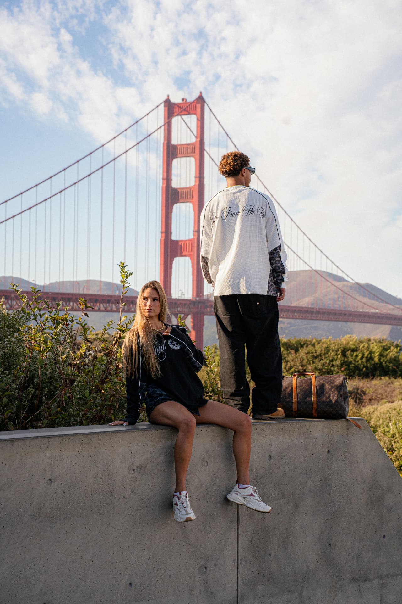 Two models wearing Voidborn black and white layers beside the Golden Gate Bridge