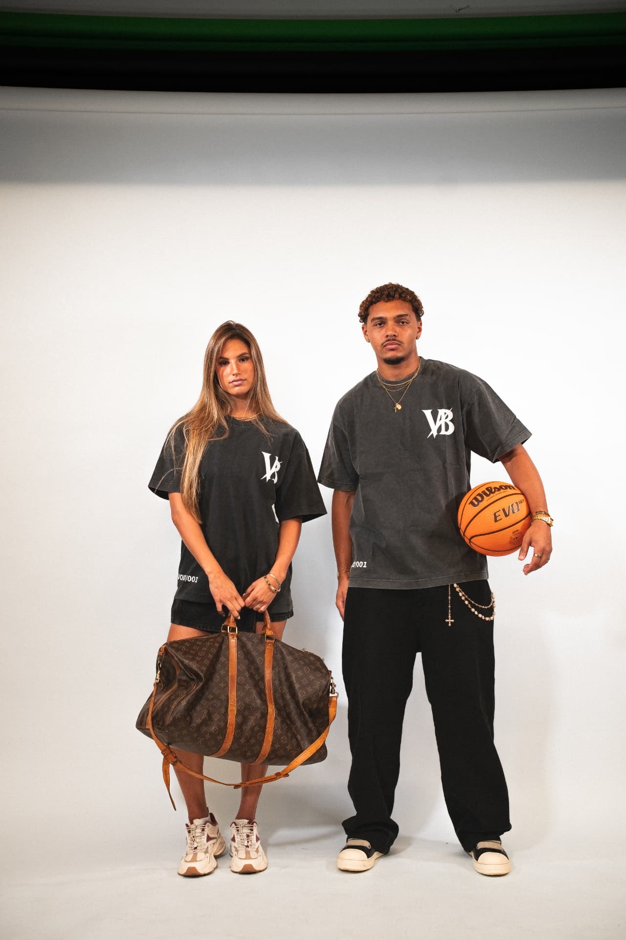 Two models in charcoal Voidborn VB tees and shorts with a basketball in the studio