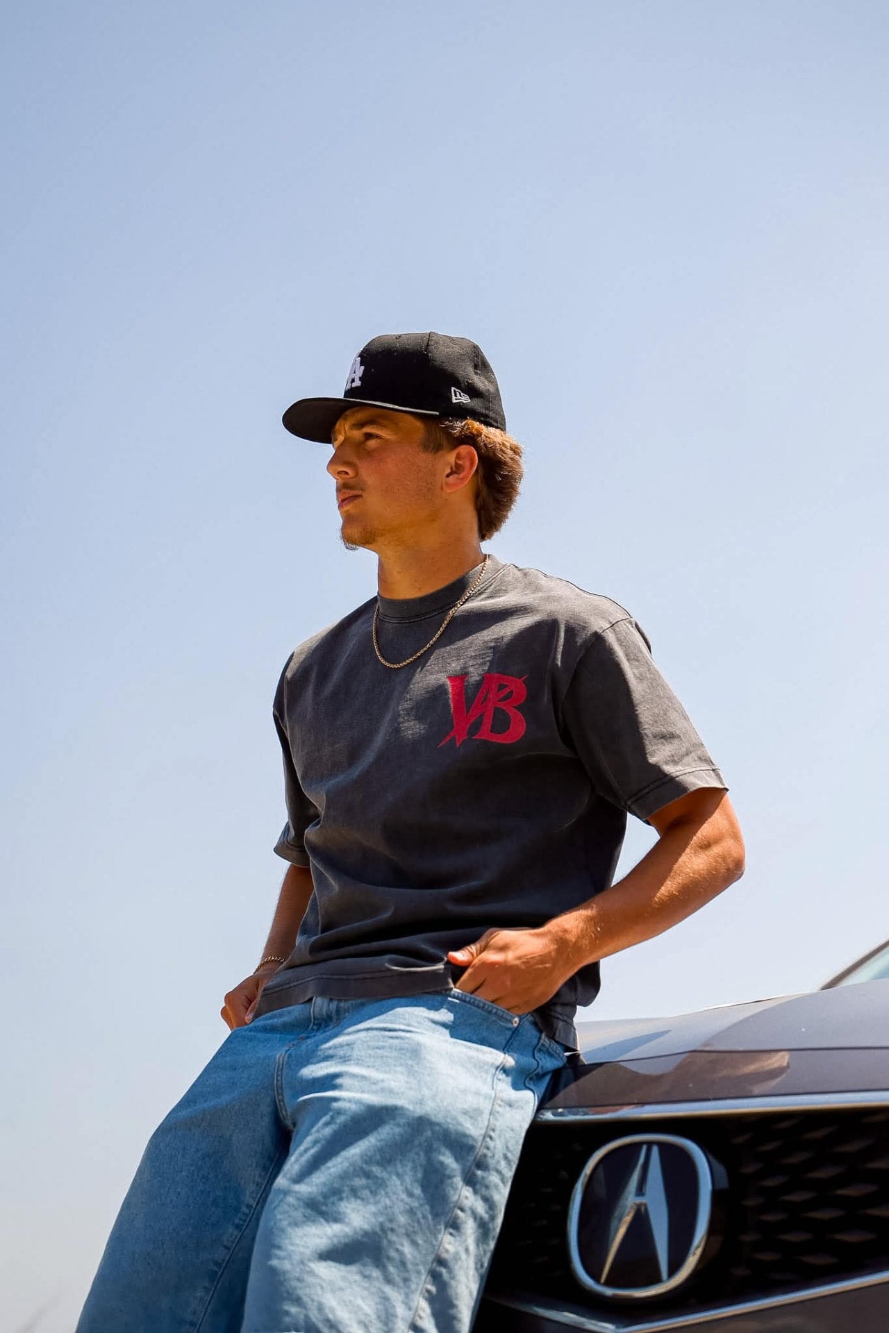 Voidborn charcoal tee with red VB monogram worn beside a car
