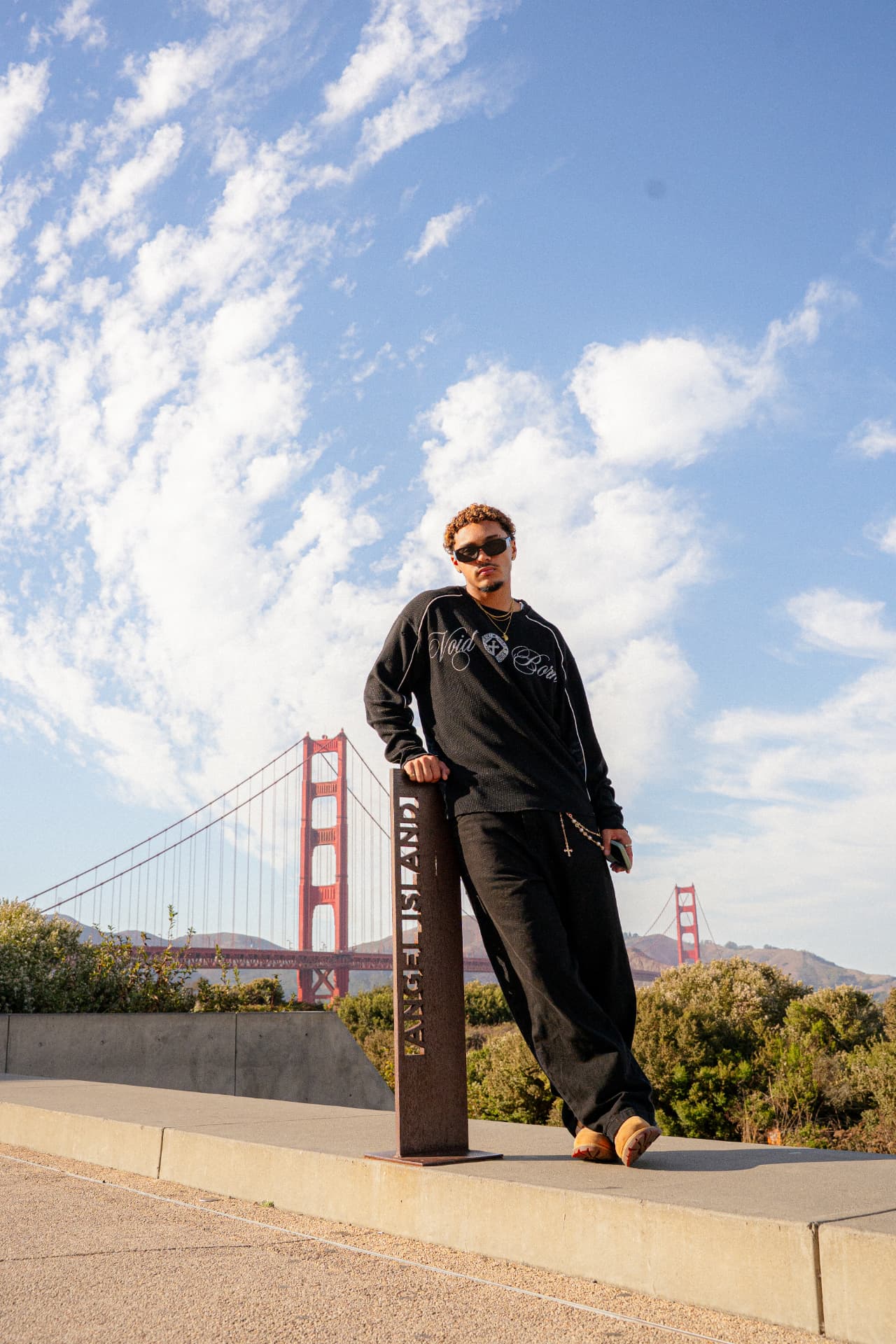 Model wearing a Voidborn black sweatshirt and dark trousers by the Golden Gate Bridge