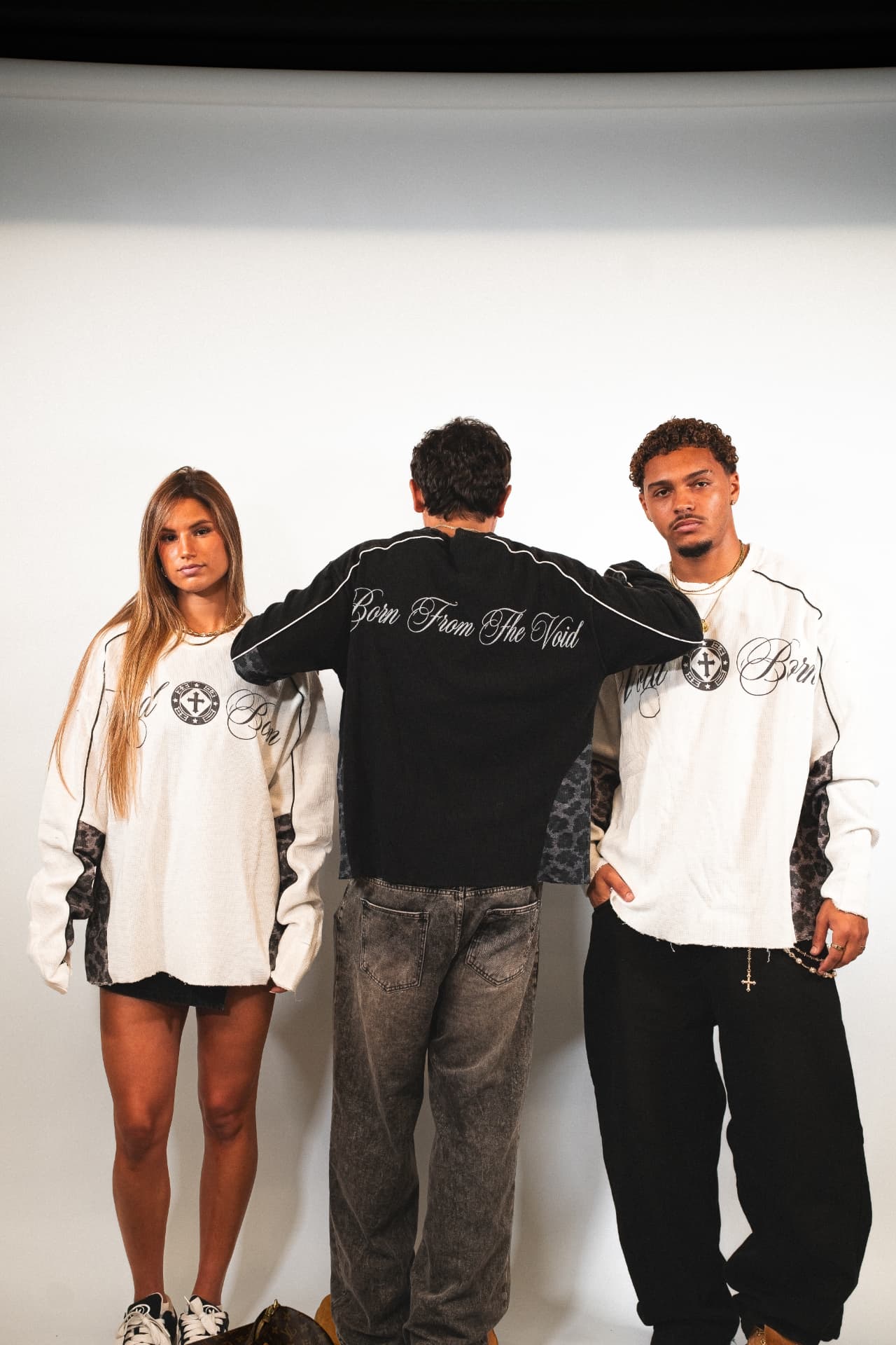 Three models in Voidborn Void Born sweaters on a studio cyclorama, one showing the Born From The Void back print